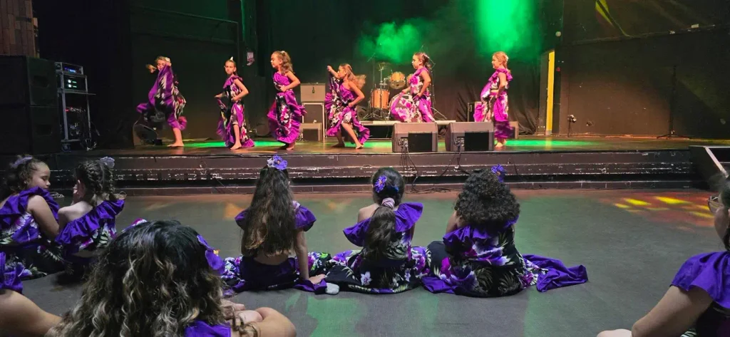 Fillettes en robes violettes dansant sur scène, d'autres assises face à elles