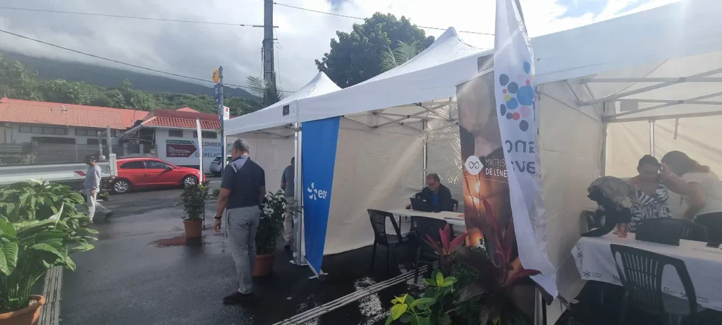 Tentes blanches des partenaires sur le parking, drapeau EDF et France travail et montagne au fond