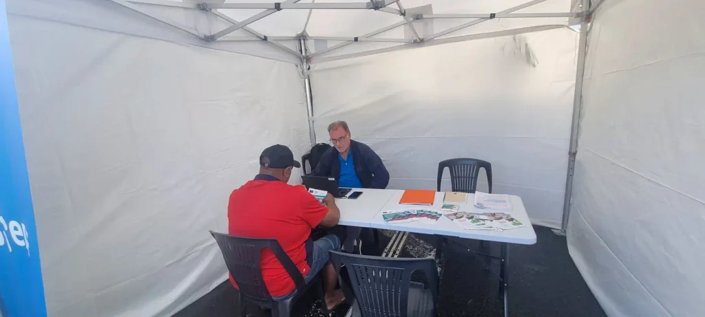 Un agent reçoit un usager à une table sous tente, ordinateur portable ouvert
