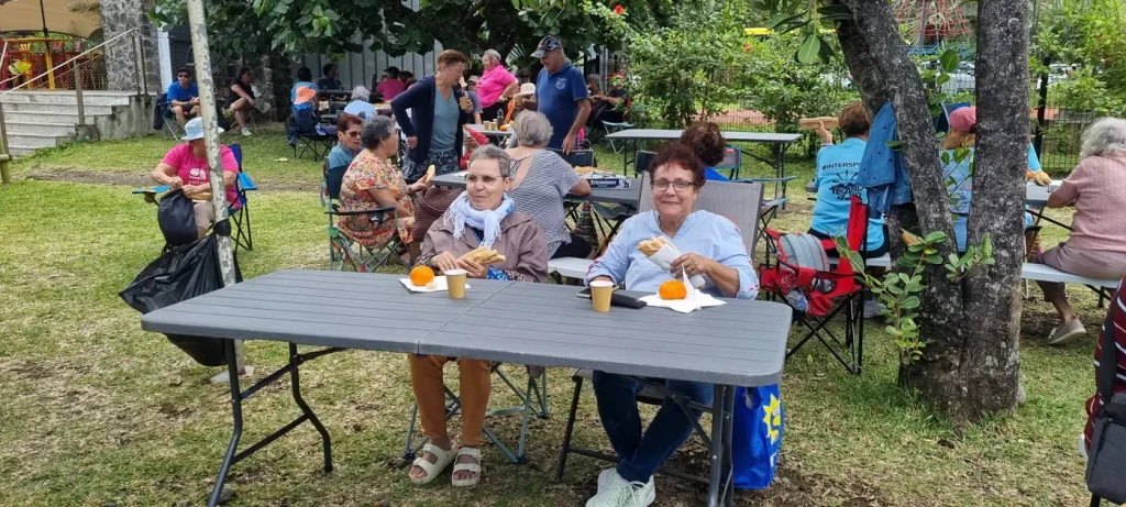 Seniors en train de pique-niquer à l'ombre des arbres, assis à des tables